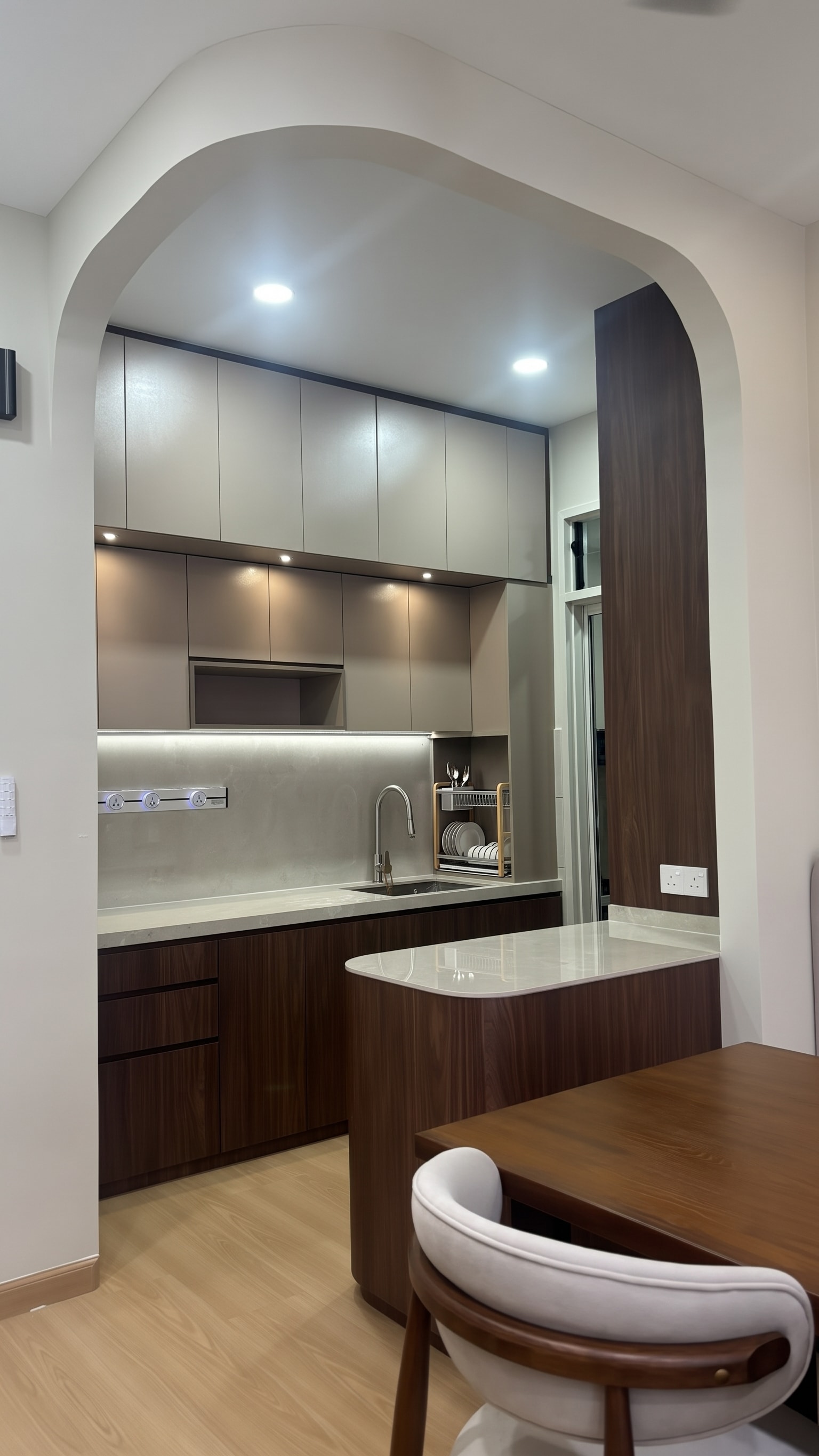Kitchen through the arch — dark walnut lower cabinets, taupe upper cabinets and curved white island