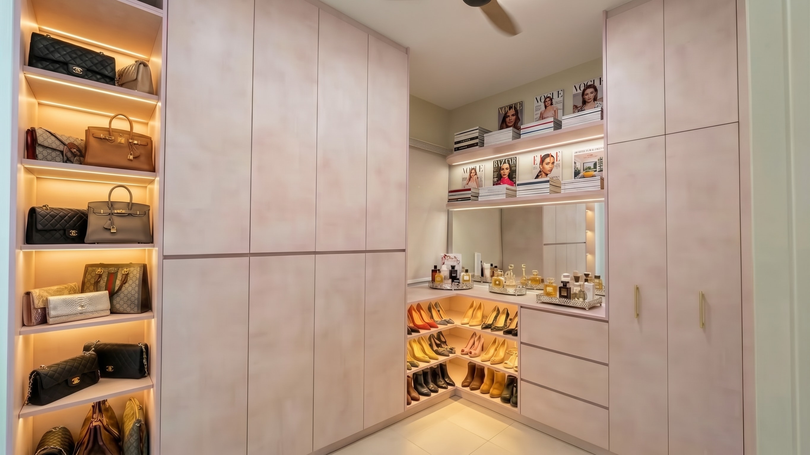 Walk-in wardrobe with blush pink cabinetry, lit designer bag shelves, heel racks and cosmetics station