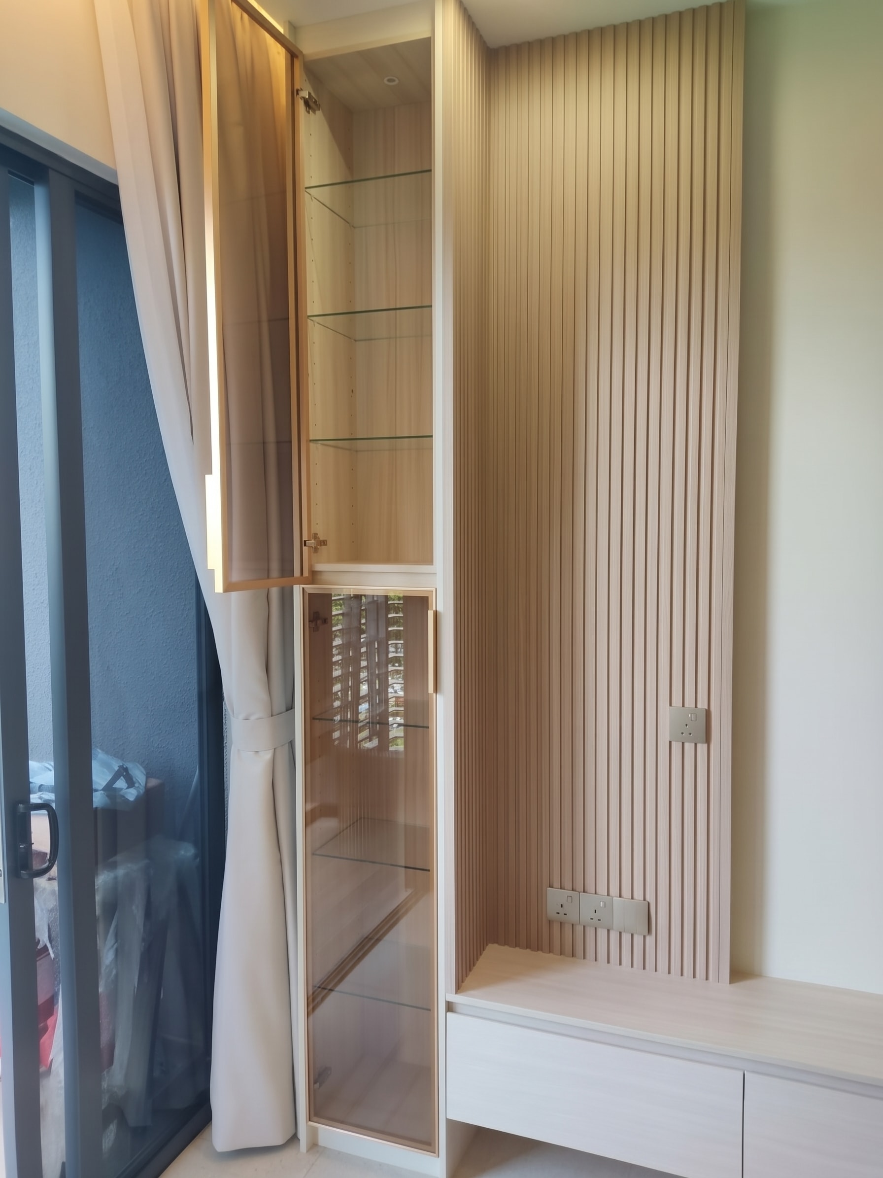 Glass-door display cabinet open showing glass shelves and fluted wall panel detail